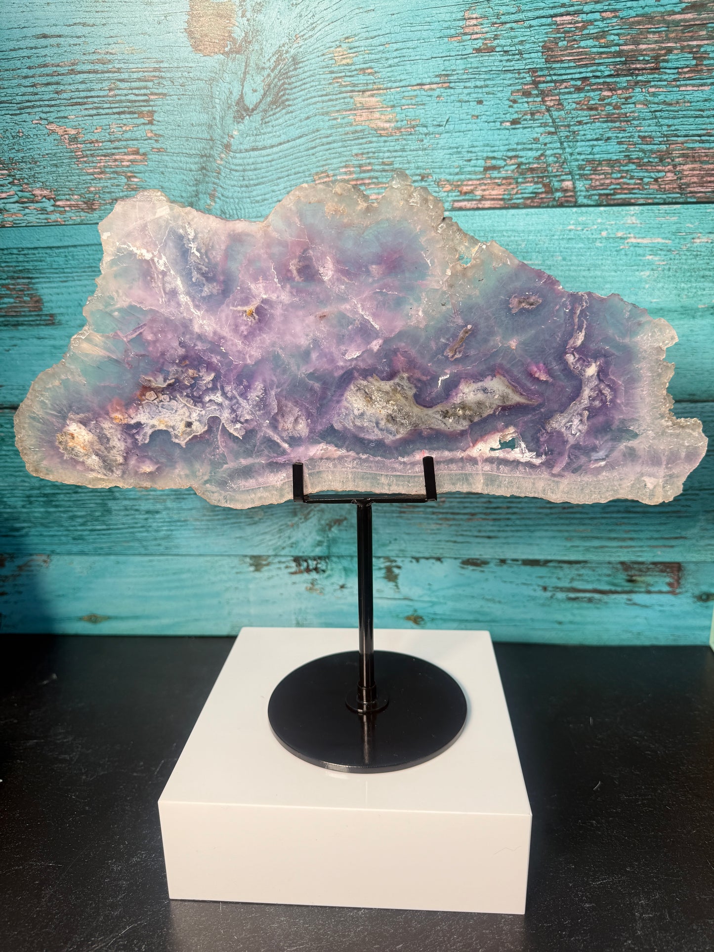Pink, purple, and blue Fluorite crystal slab on a modern black stand, used as elegant home decor